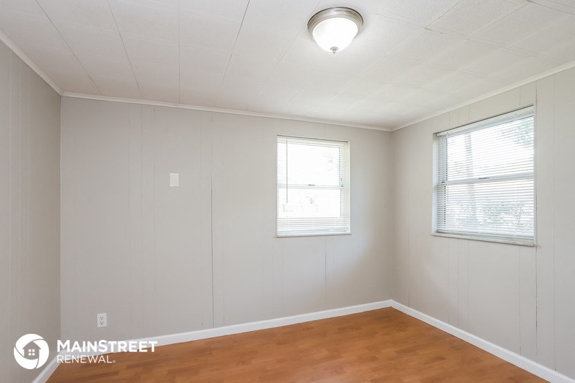 the living room of a house with wood flooring and two windows