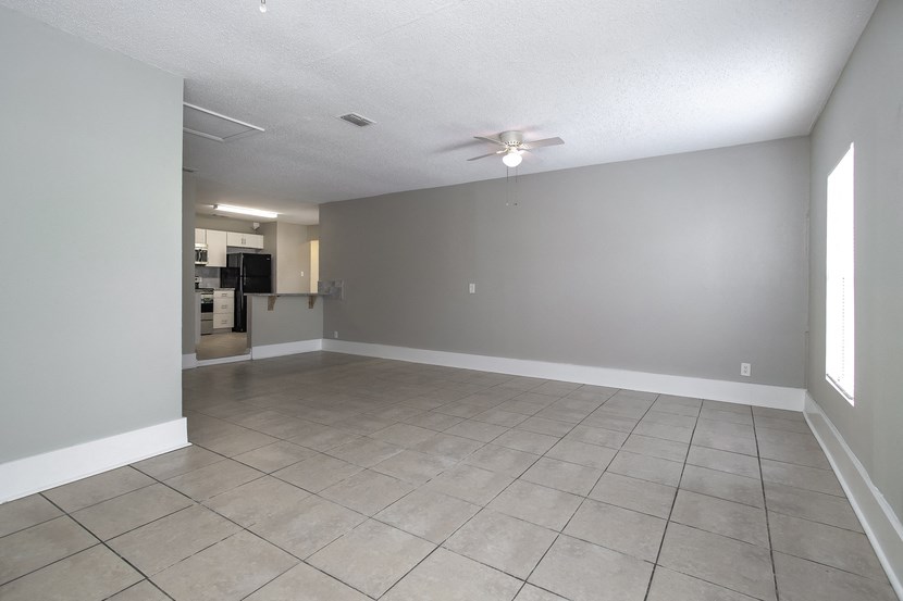 an empty living room with tile flooring and a ceiling fan