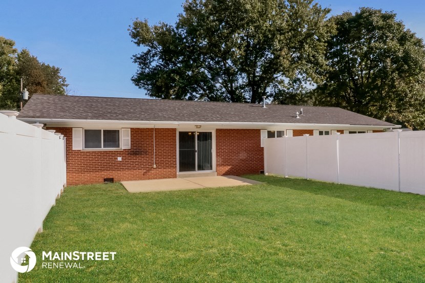 the front of a brick house with a lawn and a white fence