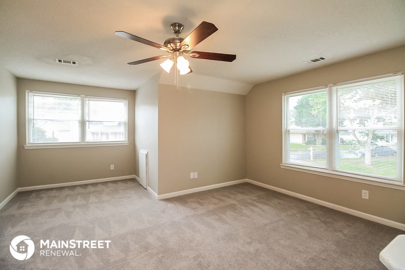 an empty living room with a ceiling fan and two windows