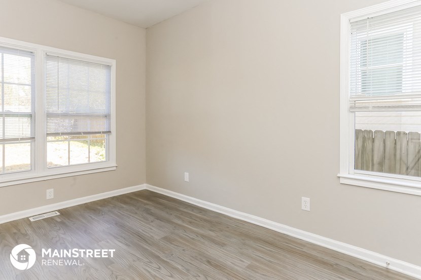 a bedroom with wood flooring and two windows