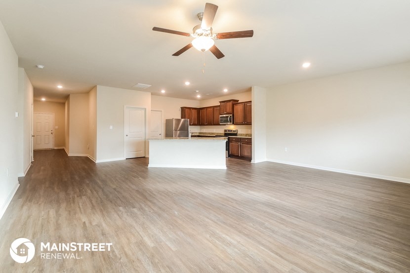 the living room and kitchen of an apartment with wood flooring and a ceiling fan