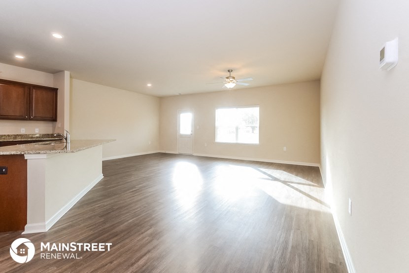 an empty living room with a kitchen and a ceiling fan