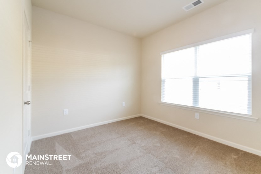 a bedroom with a large window and beige carpeting