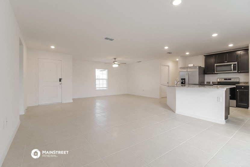 an empty living room and kitchen with white tile flooring and a counter