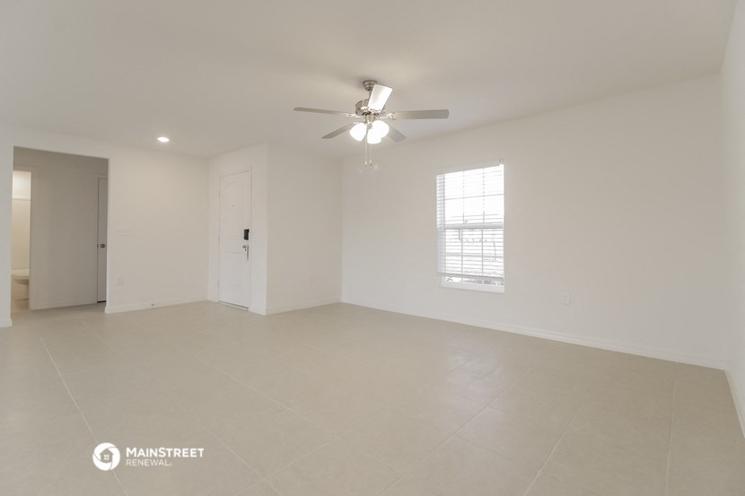 a spacious living room with white walls and a ceiling fan