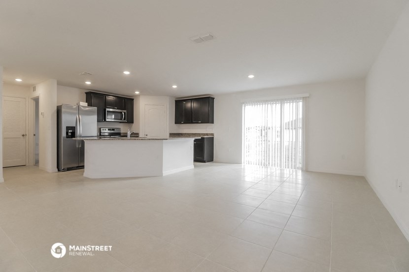 an open kitchen and living room with white tile flooring and a white counter top