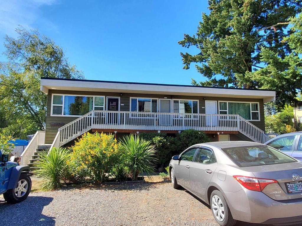 A silver car is parked in front of a house with a porch.