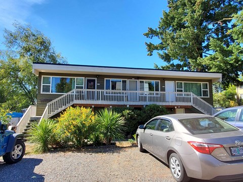 A silver car is parked in front of a house with a porch.