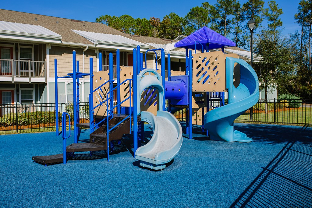 a playground with a blue playset and slides in front of a house