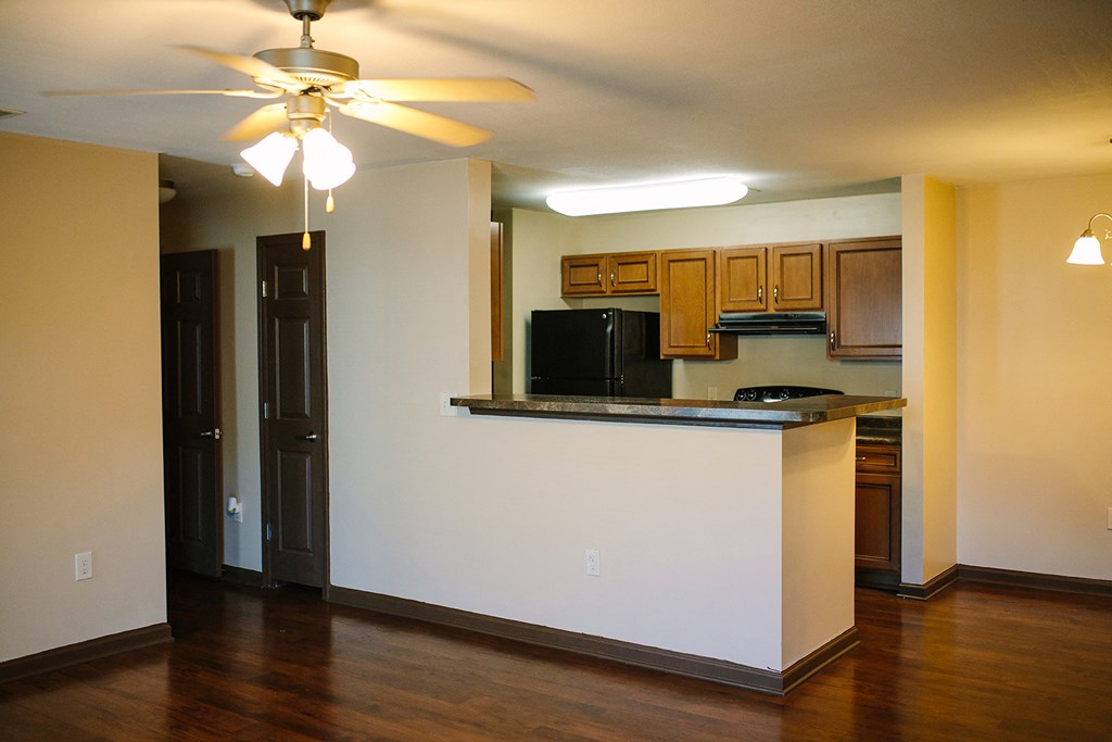 an empty living room with a kitchen and a ceiling fan