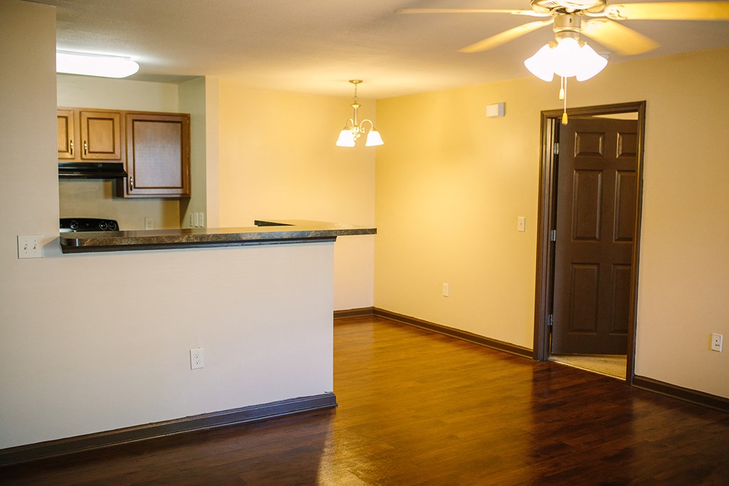 an empty living room with a kitchen and a ceiling fan