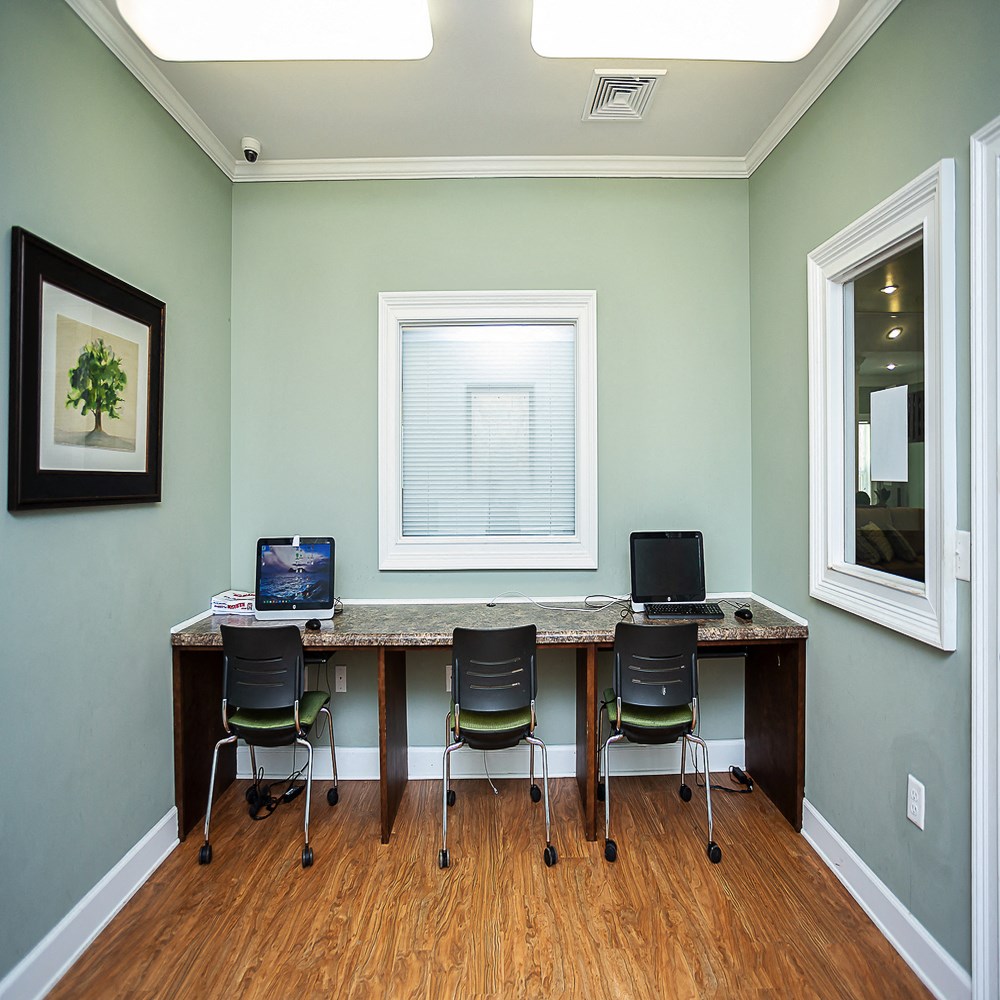 a home office with a long desk with three chairs and a window