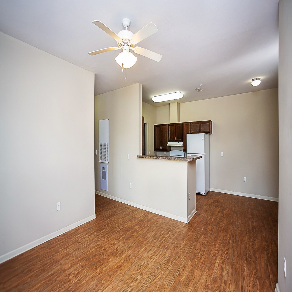 an empty living room with a kitchen and a ceiling fan