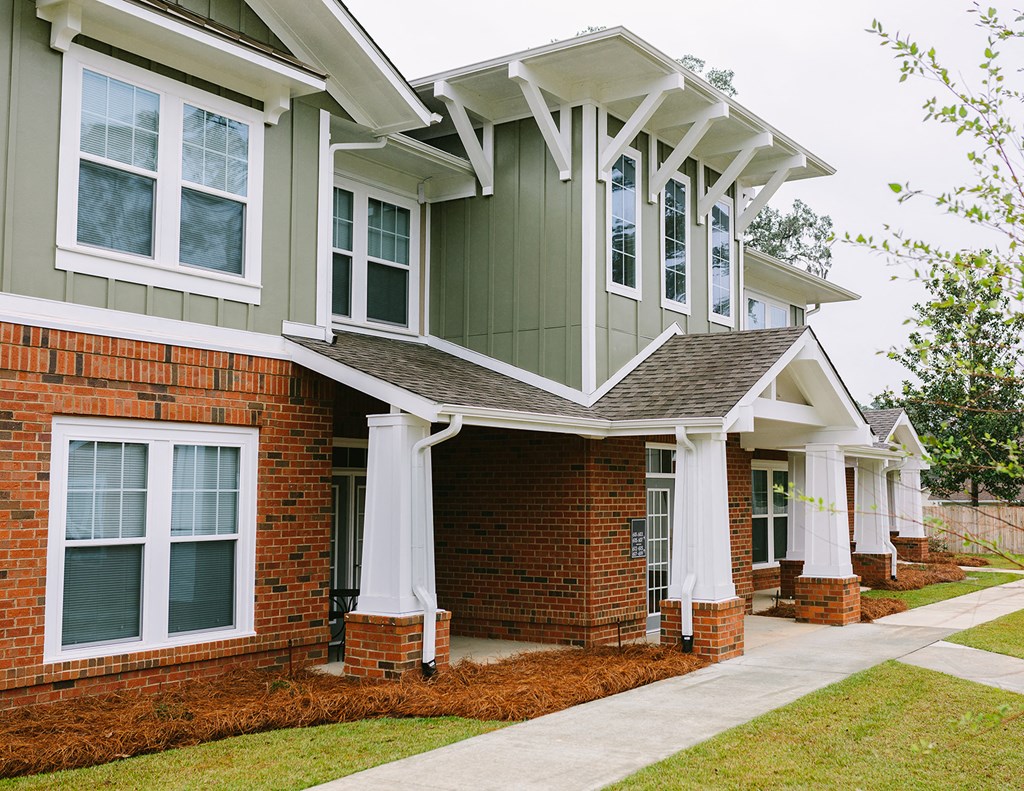 a brick house with green siding and white columns