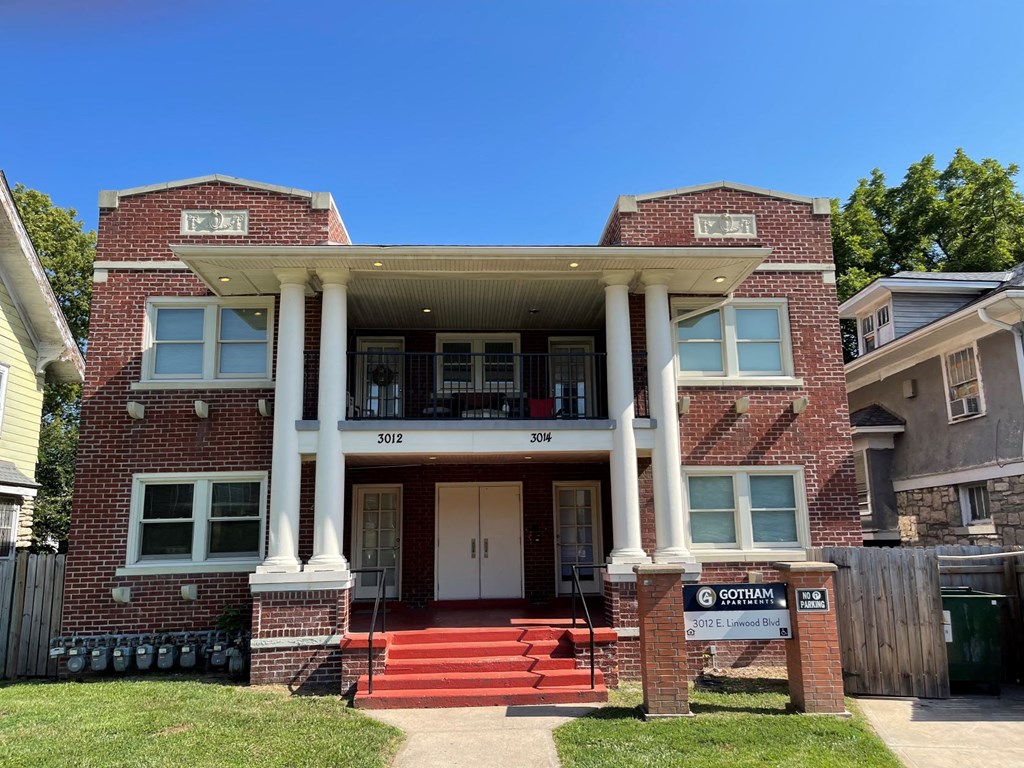 a red brick house with white pillars and a sign in front