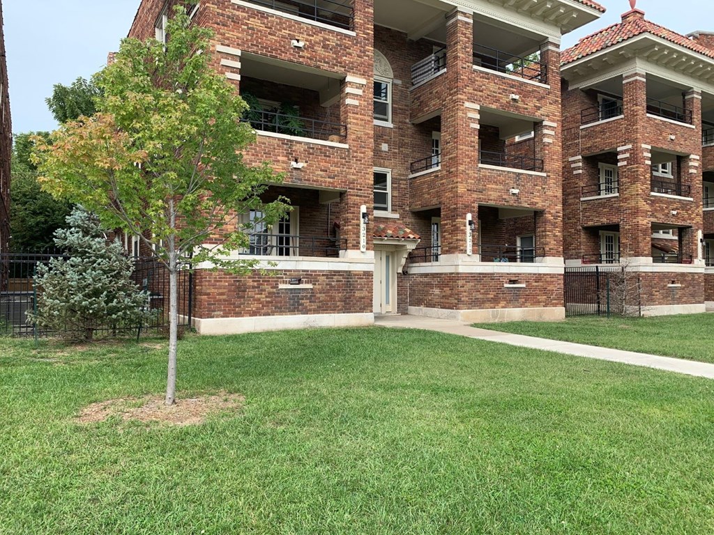 an apartment building with a lawn and a tree in front of it
