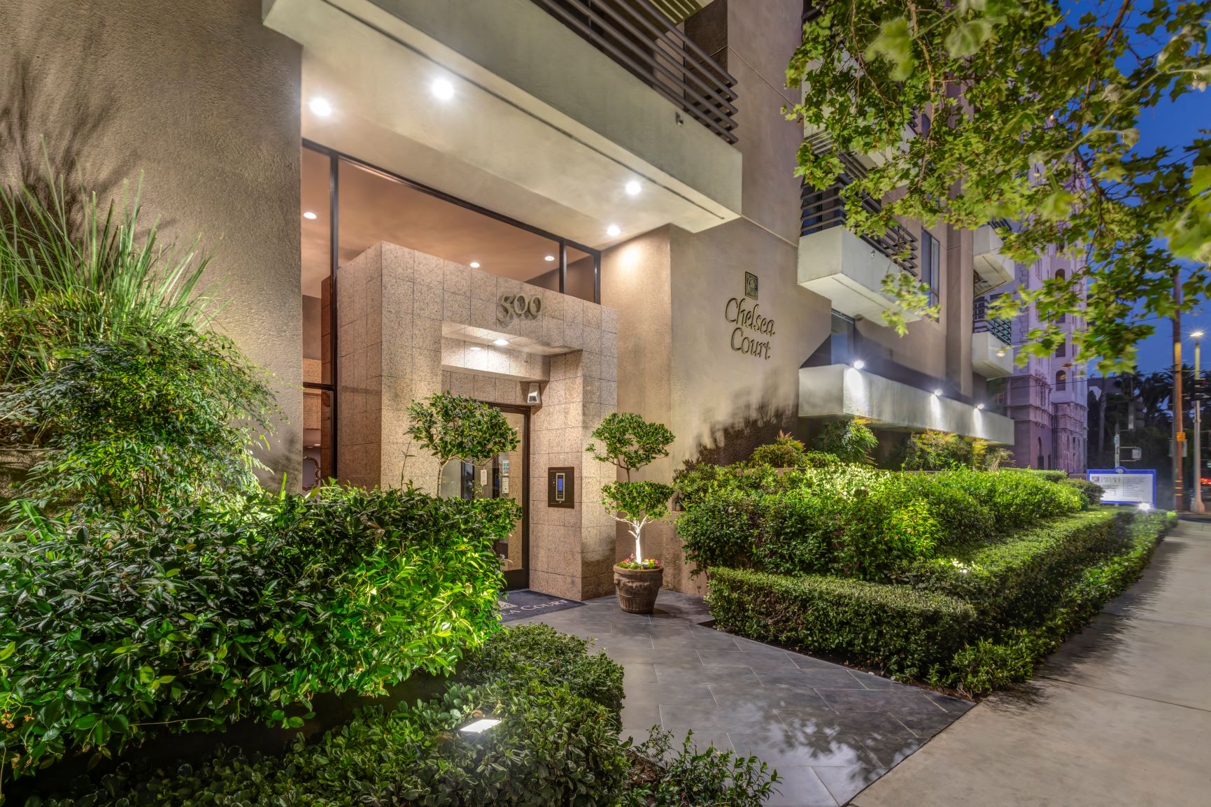 Apartments in Hancock Park, CA - Night View of Main Building Entrance Lit Up and Foliage