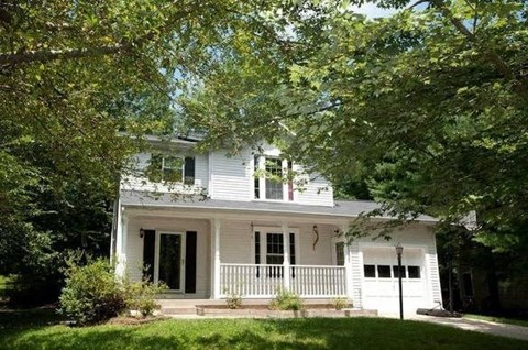 A white house with a porch and a tree in front.