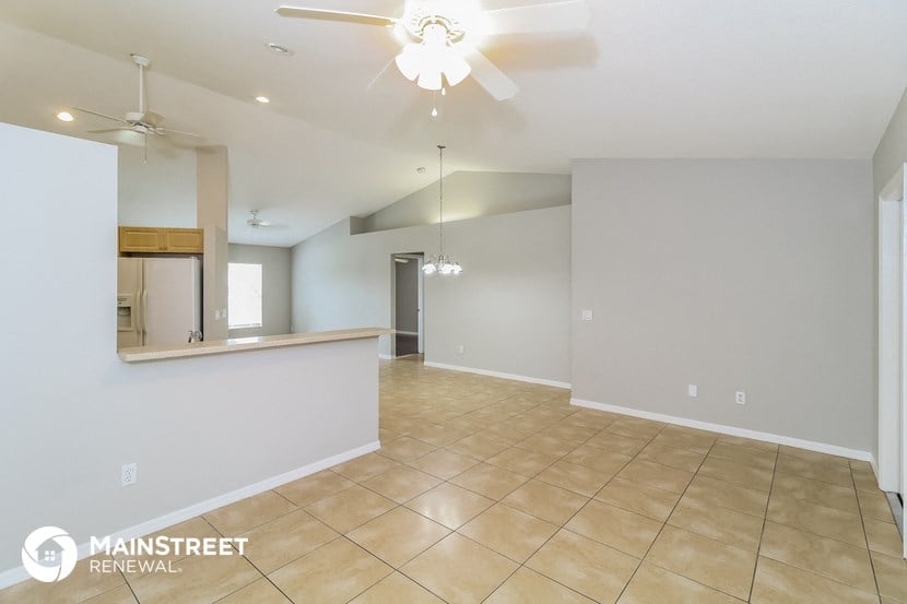 an empty living room with a kitchen and a ceiling fan