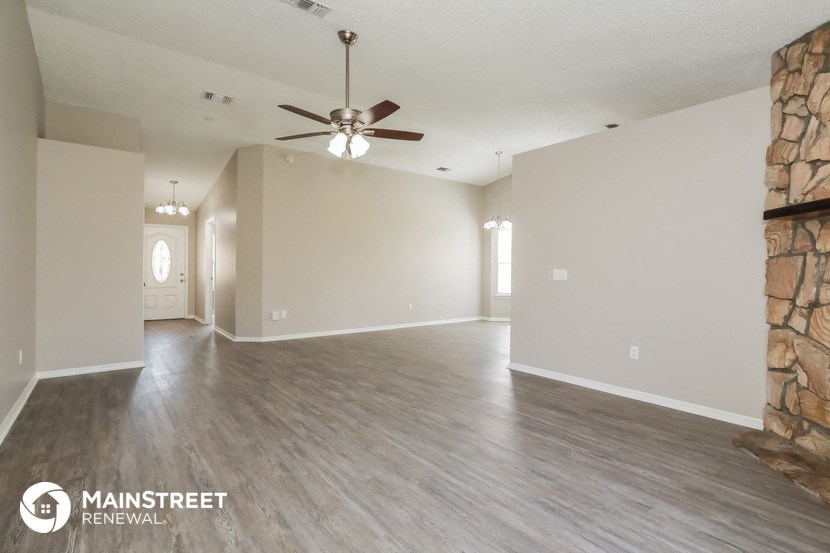 an empty living room with a ceiling fan and a stone wall