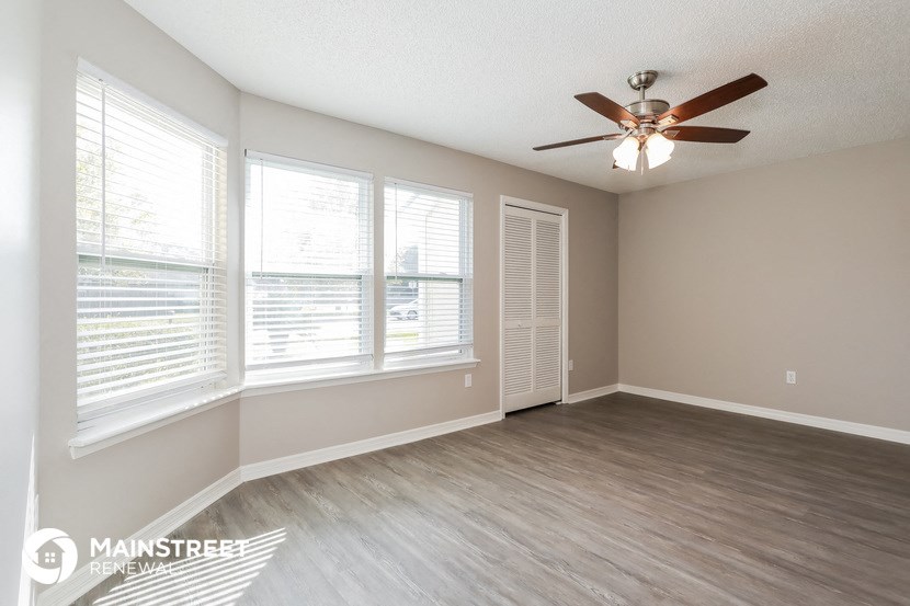the spacious living room with large windows and a ceiling fan