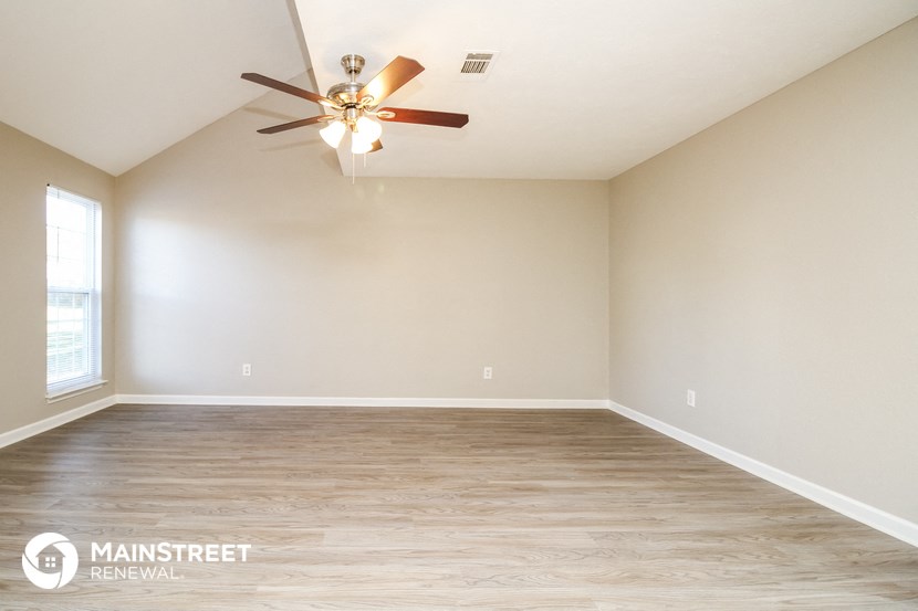 the spacious living room with white walls and a ceiling fan