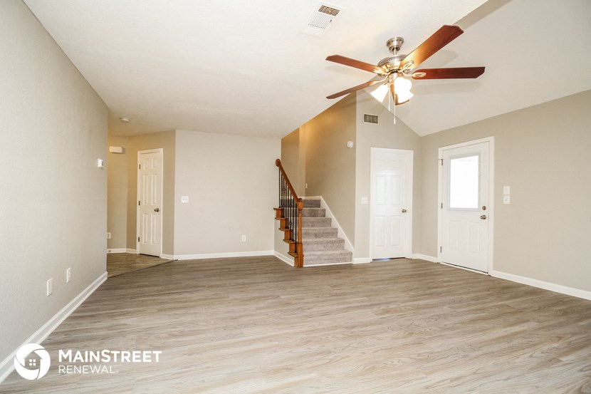 an empty living room with a ceiling fan and a staircase