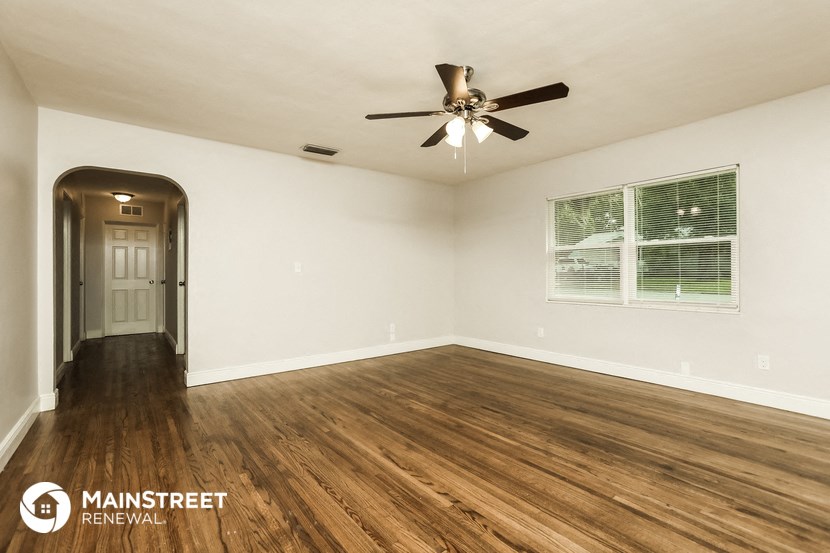 the spacious living room with hardwood flooring and a ceiling fan