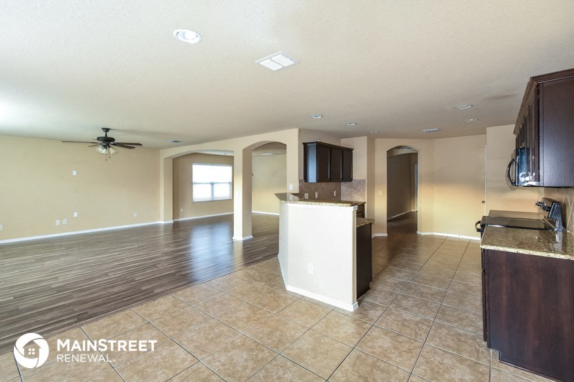 an empty living room with a kitchen and a ceiling fan
