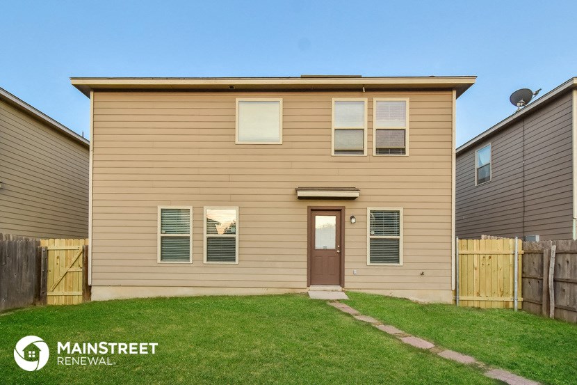 the front of a tan house with a yard and a wooden fence