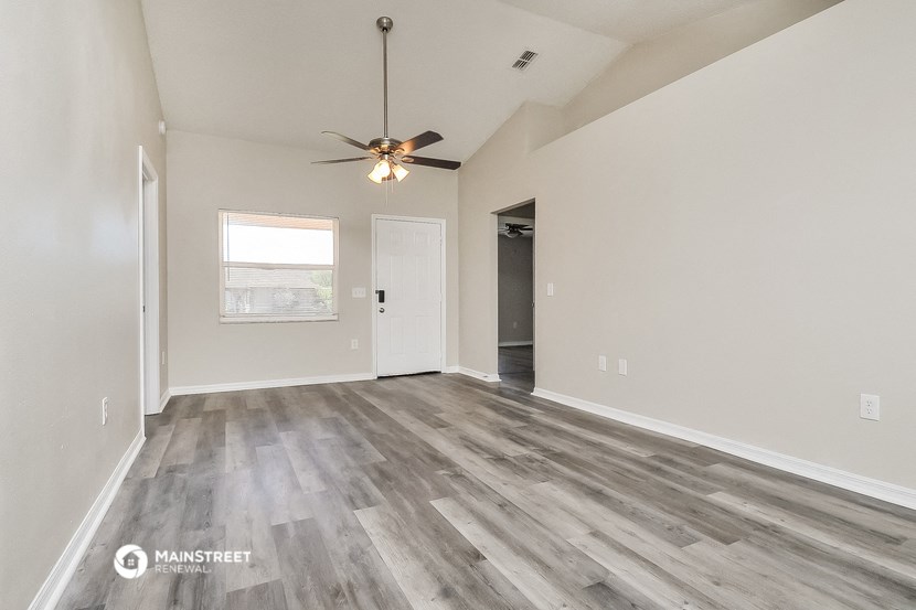 the spacious living room with wood flooring and a ceiling fan
