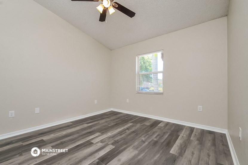 the spacious living room with wood flooring and a ceiling fan