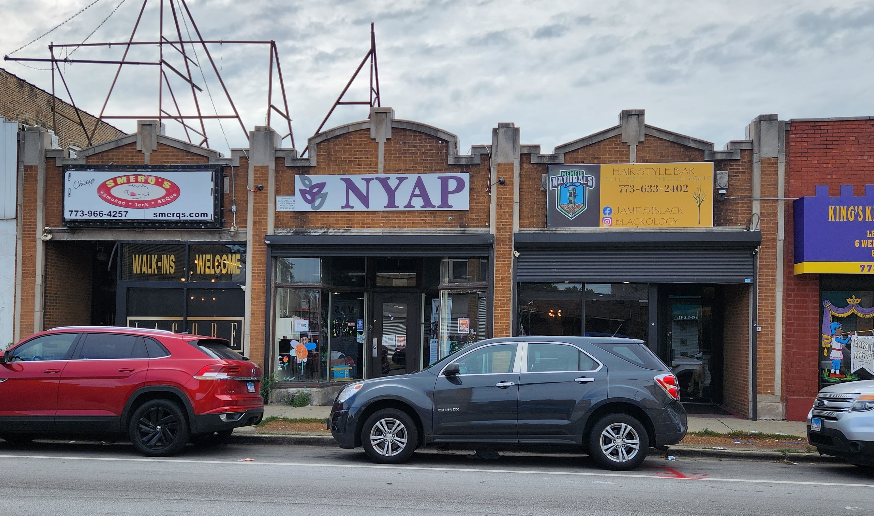 Two cars are parked in front of a building with a sign that reads "NYAP.".