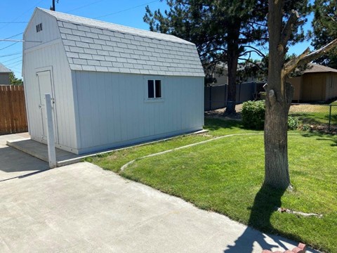 A small white shed with a grey roof is situated in a grassy area.