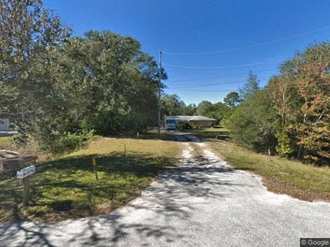 A gravel road leads to a house surrounded by trees.
