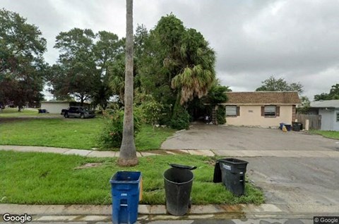 A street view with a blue trash can and a black trash can.
