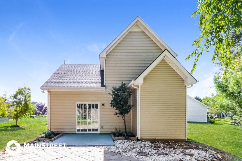 a small yellow house with a driveway and a tree