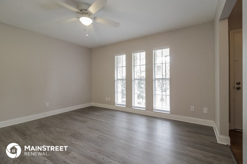 the spacious living room with wood flooring and a ceiling fan