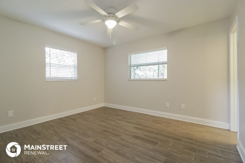 the spacious living room with wood flooring and a ceiling fan