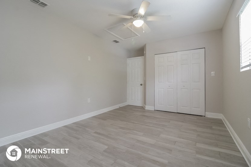 the spacious living room with white walls and a ceiling fan
