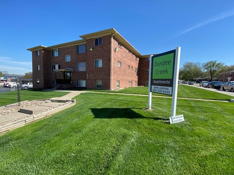 A sign for Dundee Creek Apartments stands in front of a brick building.