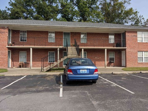 A blue car is parked in a parking lot in front of a brick apartment building.