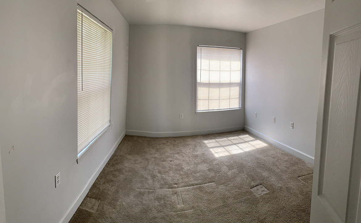 an empty living room with two windows and a carpet