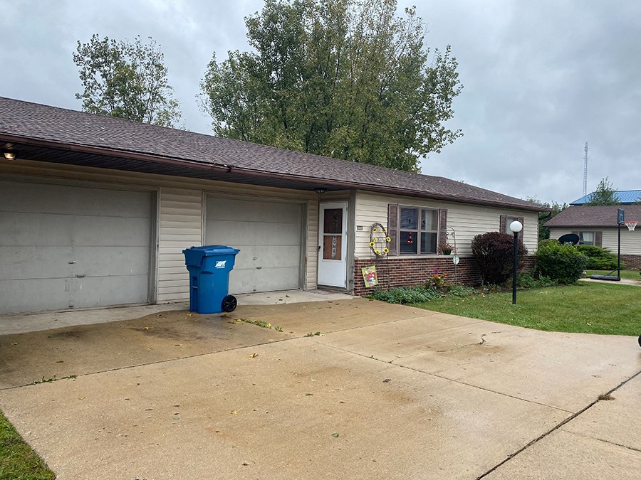 a white house with a driveway and a blue trash can