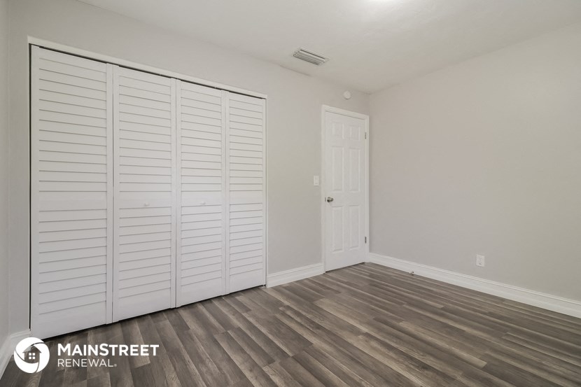 the closet in a bedroom with white shutters and wood flooring