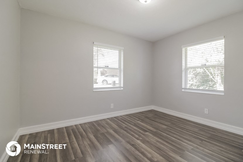 the interior of an empty room with wood flooring and two windows