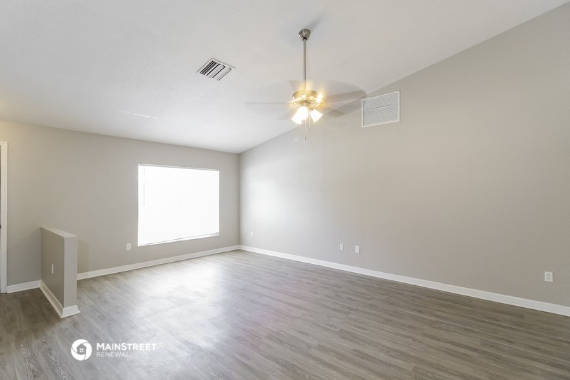 the spacious living room with wood flooring and a ceiling fan
