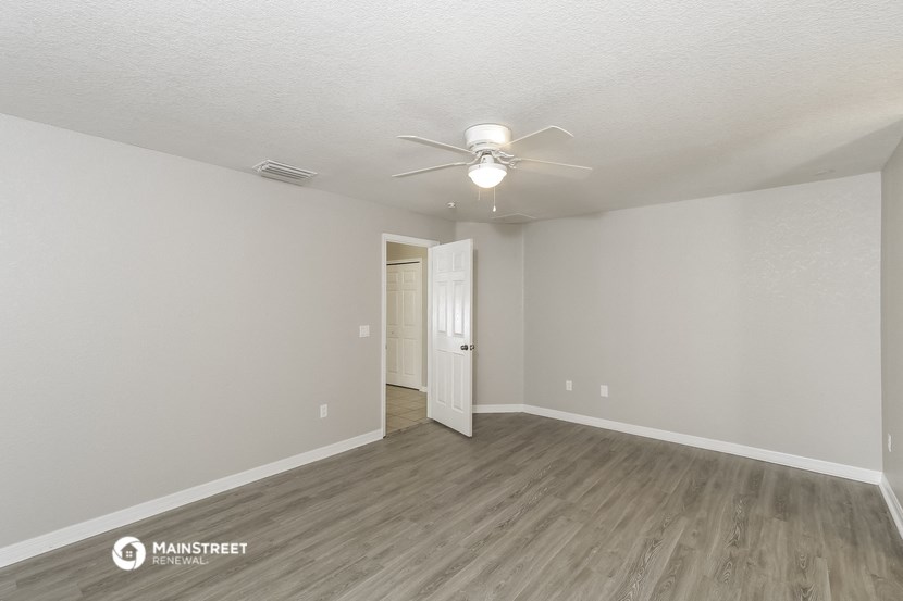 the spacious living room with white walls and a ceiling fan