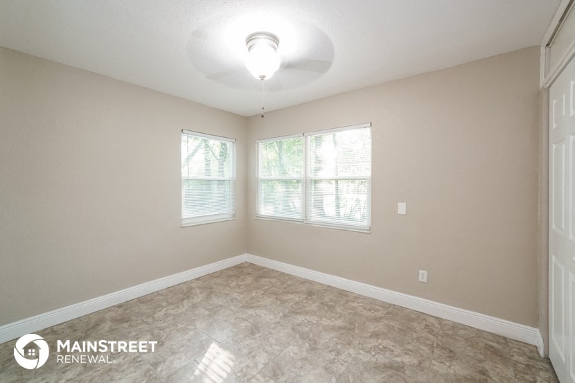 the spacious living room with two windows and a ceiling fan